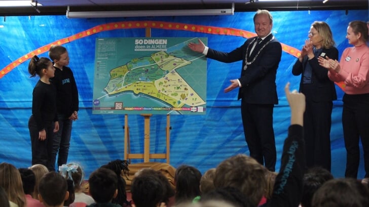 Op basisschool De Ark onthulde burgemeester Hein van der Loo samen met leerlingen Adriana en Benjamin de poster '50 dingen doen in Almere'.