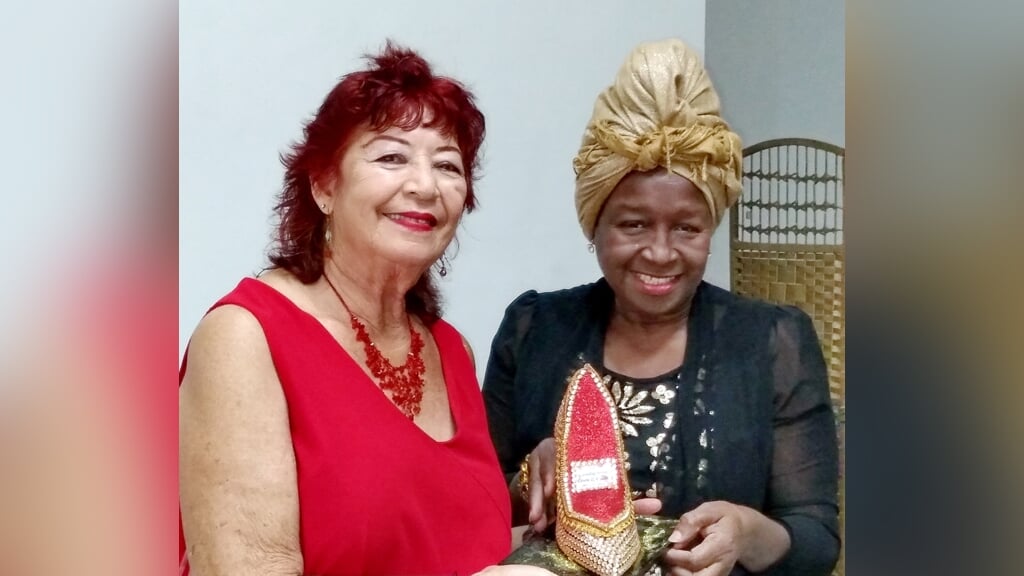 On the picture from at left 2021 Outstanding Woman Laura Quast with the symbolic high heel shoe, an artistic expression to show how high this Outstanding Woman stood and organizer Reyna Joe.