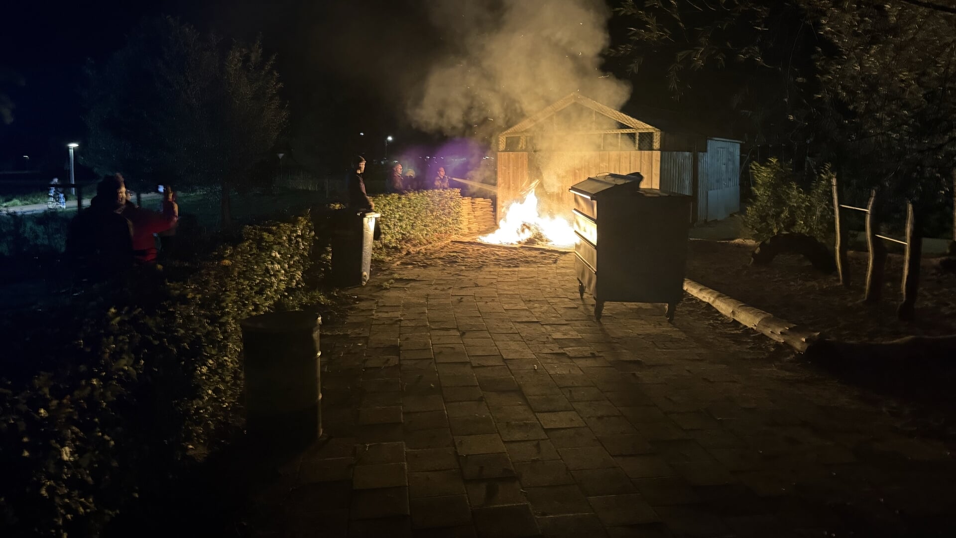 Omstanders en brandweer blussen containerbrand